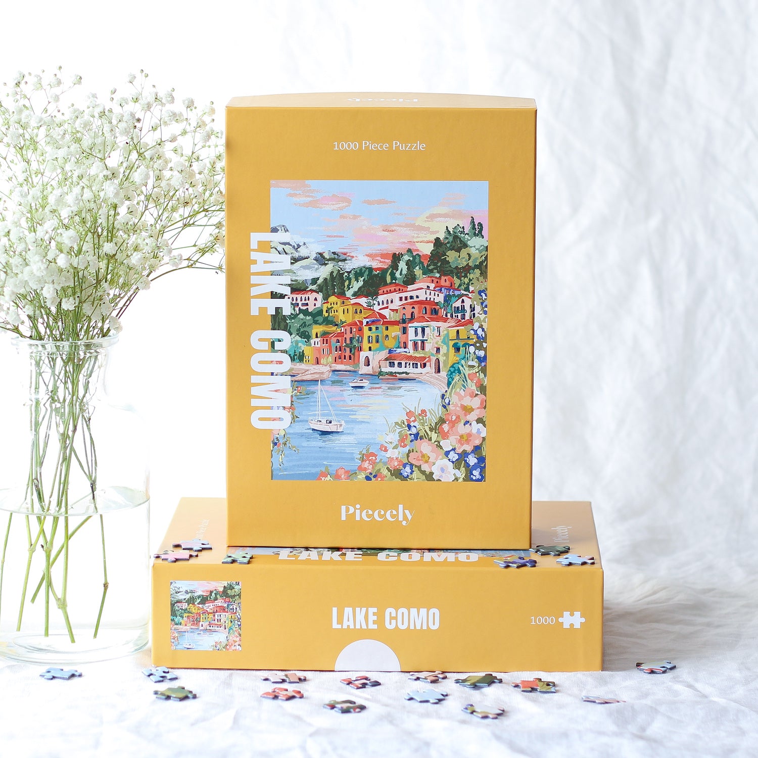 1000-teiliges Puzzle für Erwachsene, das den Comer See in Varenna zeigt. In der Bucht befinden sich zwei Boote und die Sicht auf den See ist gesäumt von bunten Häusern.