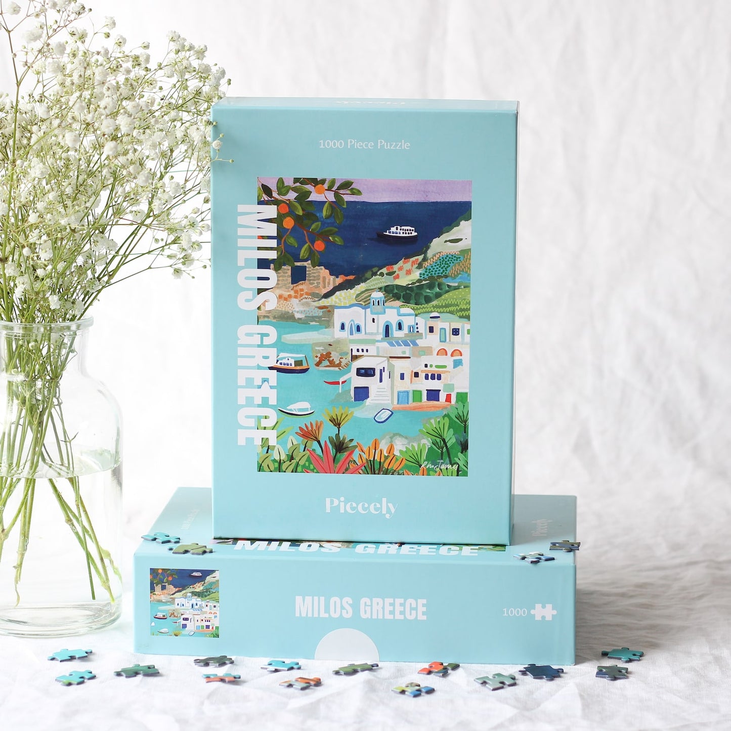 Außergewöhnliches 1000-Teile-Puzzle für Erwachsene, das einen Teil der griechischen Insel Milos zeigt. Zu sehen sind weiße Häuser and der Küste, Orangenbäume und Schiffe und Boote auf dem Meer.