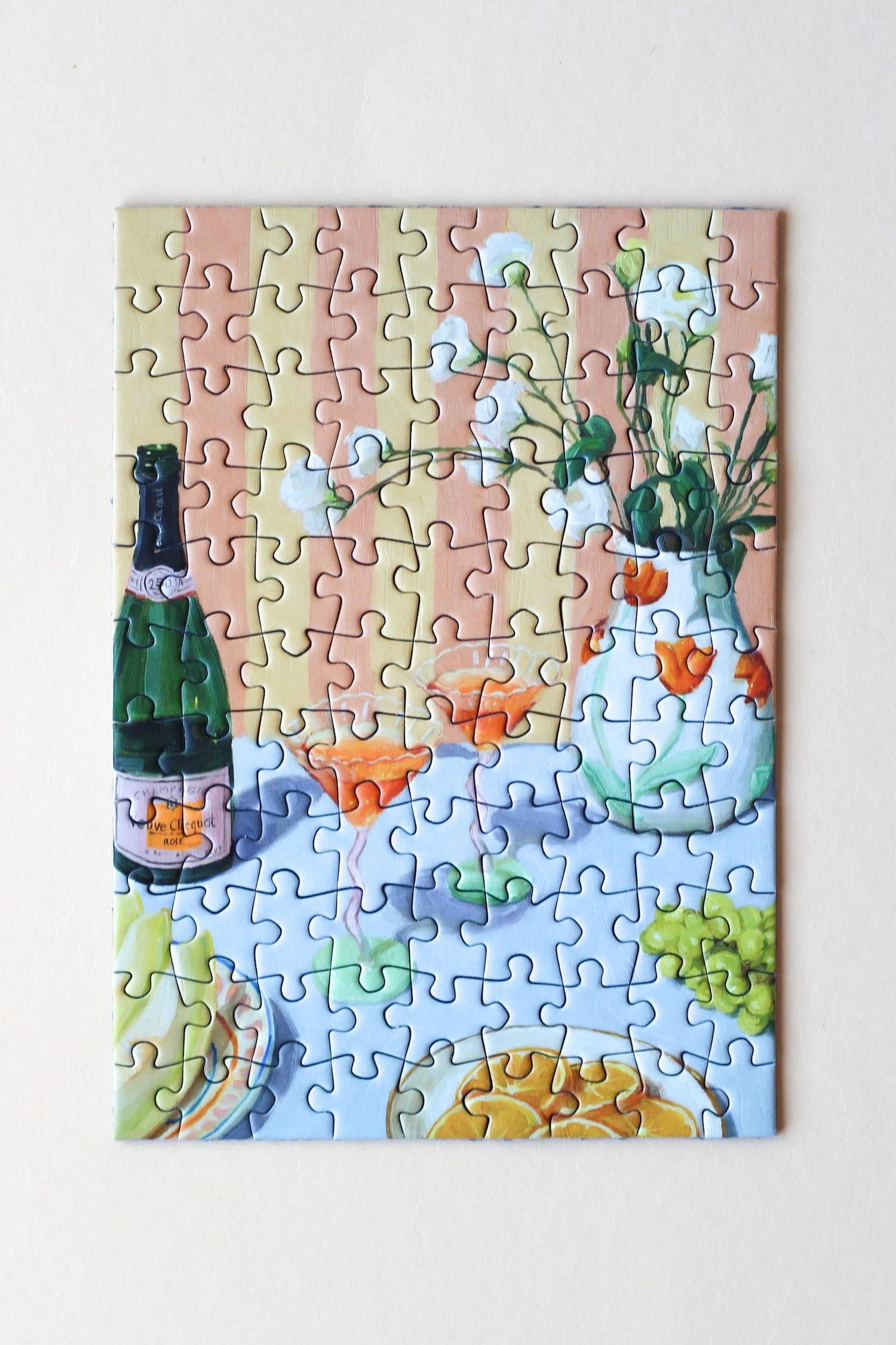 Illustration eines gedeckten Tisches mit Drinks, Orangen, Trauben und Blumen, als 99-Teile Minipuzzle ‚Love At First Sip‘ von Piecely