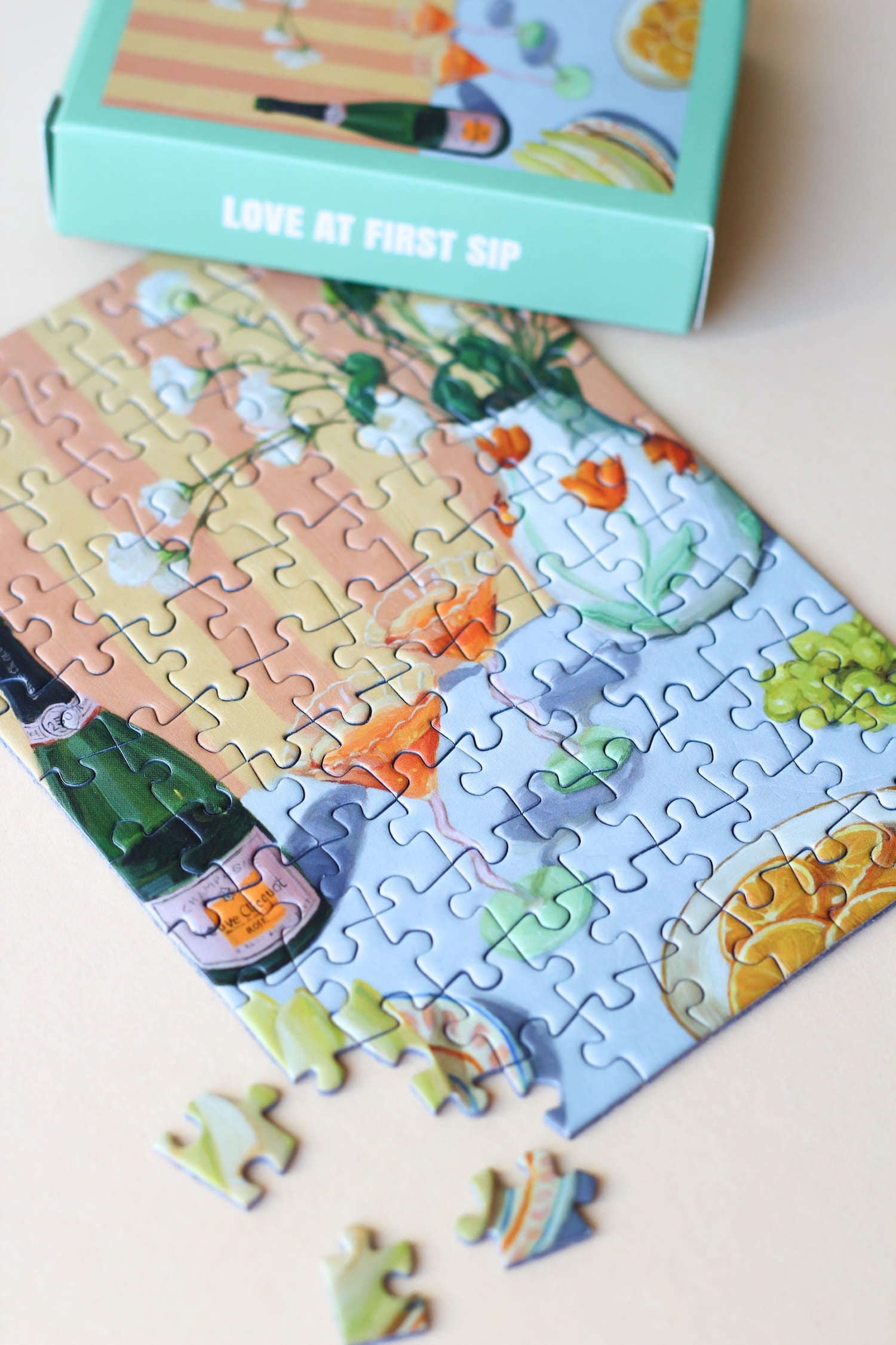 Illustration eines gedeckten Tisches mit Drinks, Orangen, Trauben und Blumen, als 99-Teile Minipuzzle ‚Love At First Sip‘ von Piecely