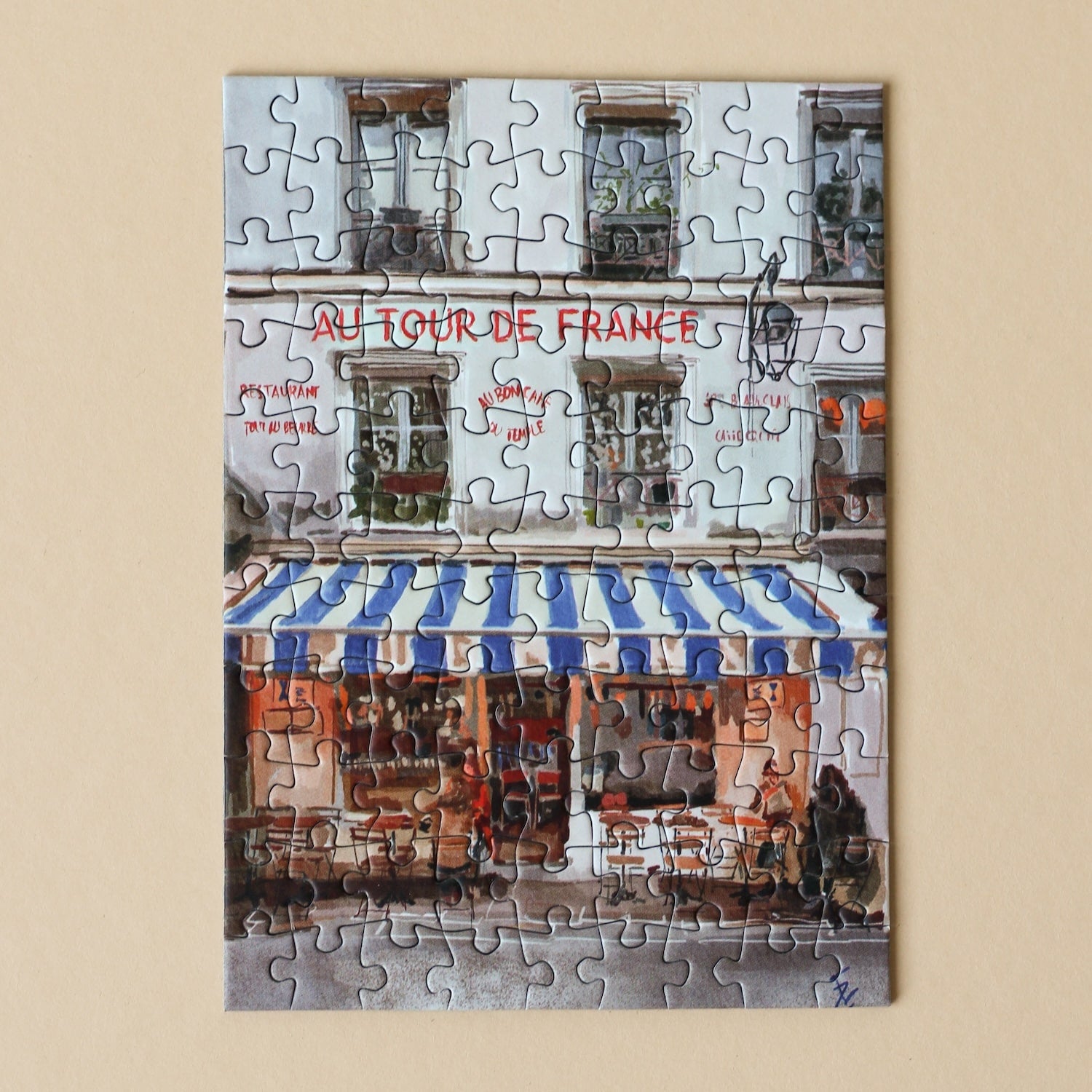 Plastikfreies Minipuzzle für Erwachsene, das ein französisches Bistro mit einer blau-weiß-gestreiften Markise zeigt.
