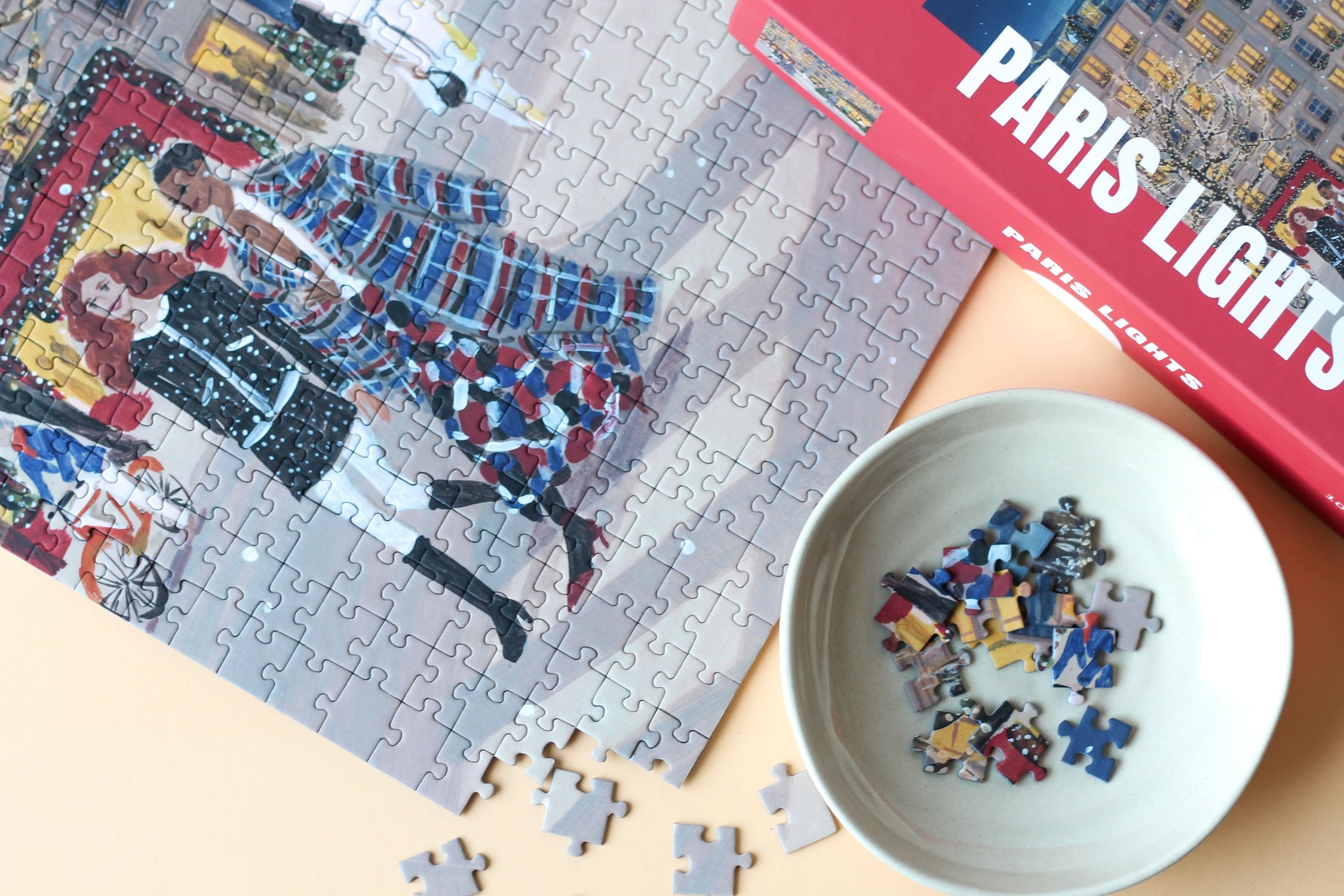 Plastikfreies Puzzle für Erwachsene, das Paris zur Weihnachtszeit zeigt. Stylisch gekleidete Menschen schlendern durch die Straßen und Bäume und Häuser sind mit leuchtenden Lichterketten geschmückt.