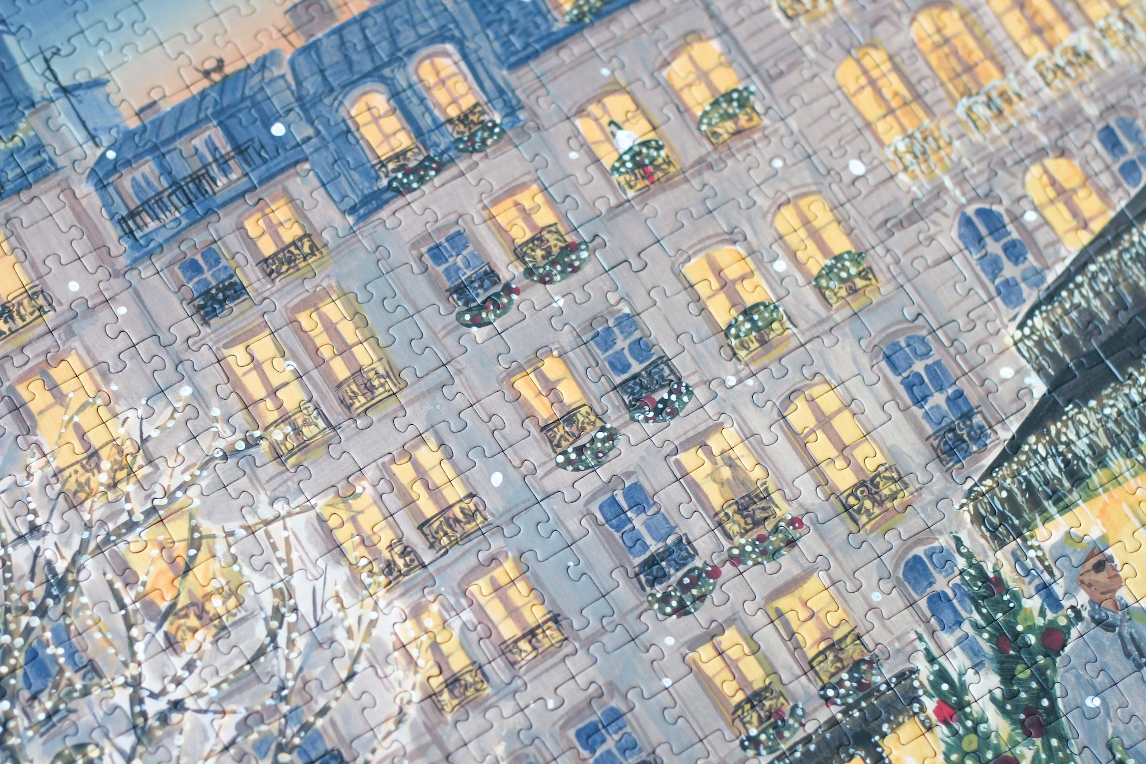 Plastikfreies Puzzle für Erwachsene, das Paris zur Weihnachtszeit zeigt. Stylisch gekleidete Menschen schlendern durch die Straßen und Bäume und Häuser sind mit leuchtenden Lichterketten geschmückt.