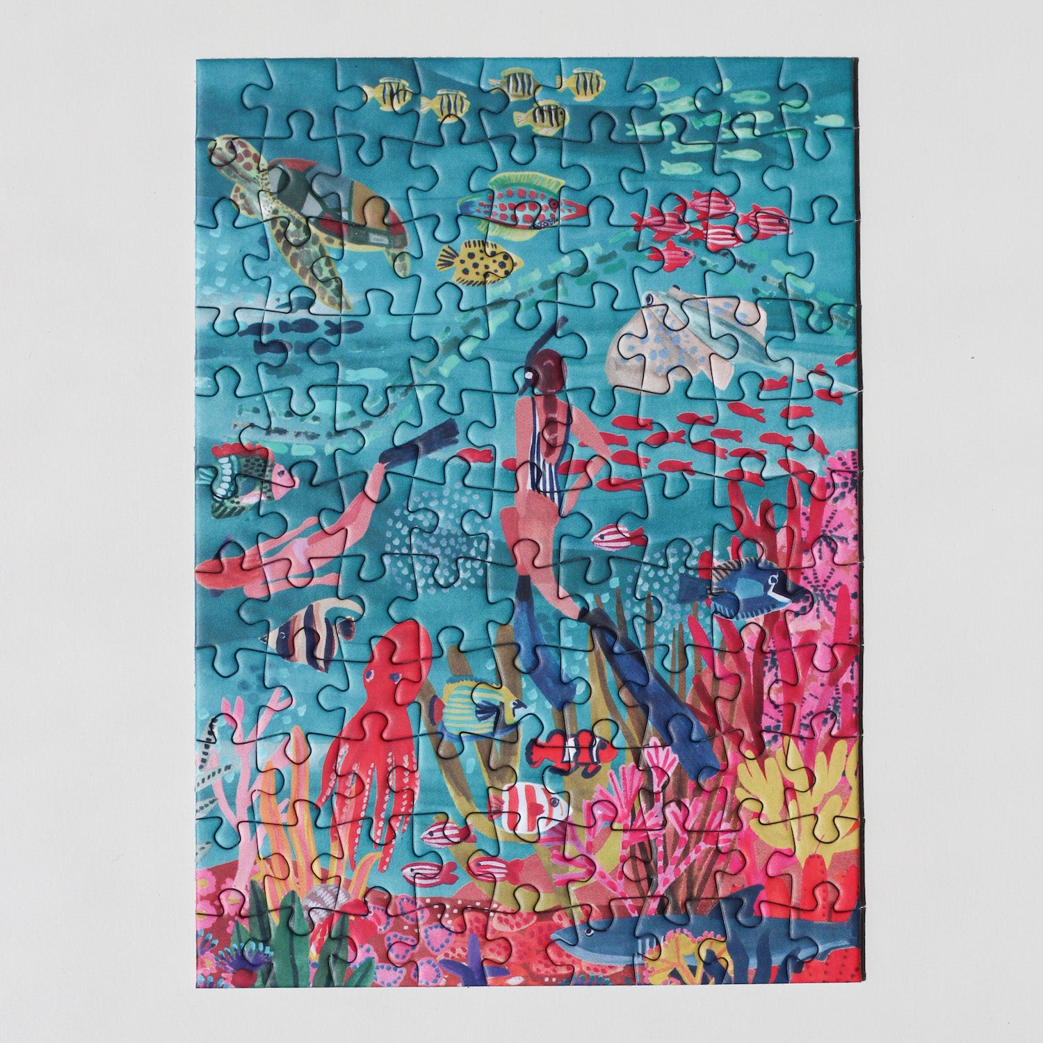 99-teiliges Under The Sea Minipuzzle für Erwachsene, das zwei Frauen beim Schnorcheln im Meer zeigt. Die Frauen sind umgeben von bunten Fischen, einem Oktopus, einem Rochen, einer Schildkröte und einem Hai.