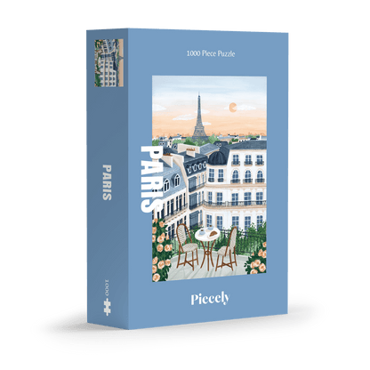 1000-Teile-Puzzle „Paris“ von Piecely – Illustration eines Pariser Balkons mit Frühstückstisch und Blick auf den Eiffelturm, auf hellblauer Verpackung.