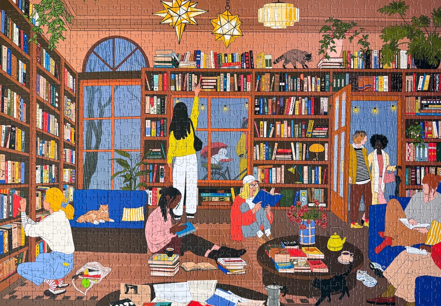 1000-Teile-Puzzle „Book Nook“ von Piecely – Illustration einer gemütlichen Bibliothek mit Bücherregalen, Lesenden und warmem Licht, auf brauner Verpackung.