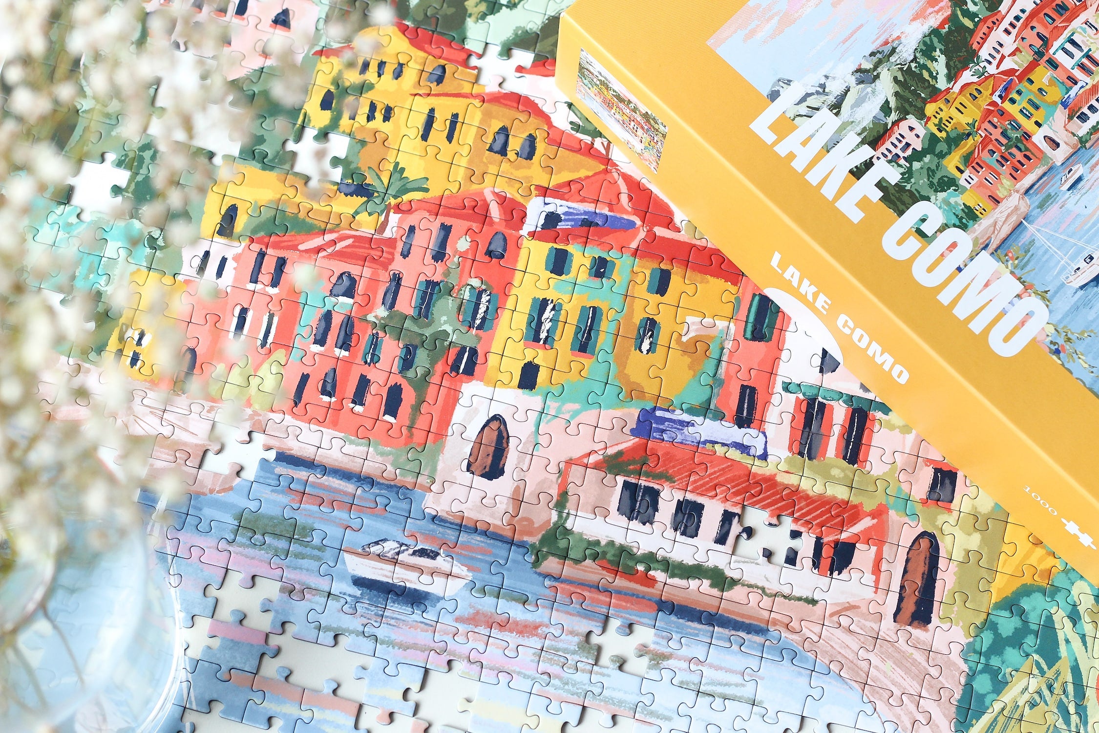 1000-teiliges Puzzle für Erwachsene, das den Comer See in Varenna zeigt. In der Bucht befinden sich zwei Boote und die Sicht auf den See ist gesäumt von bunten Häusern.