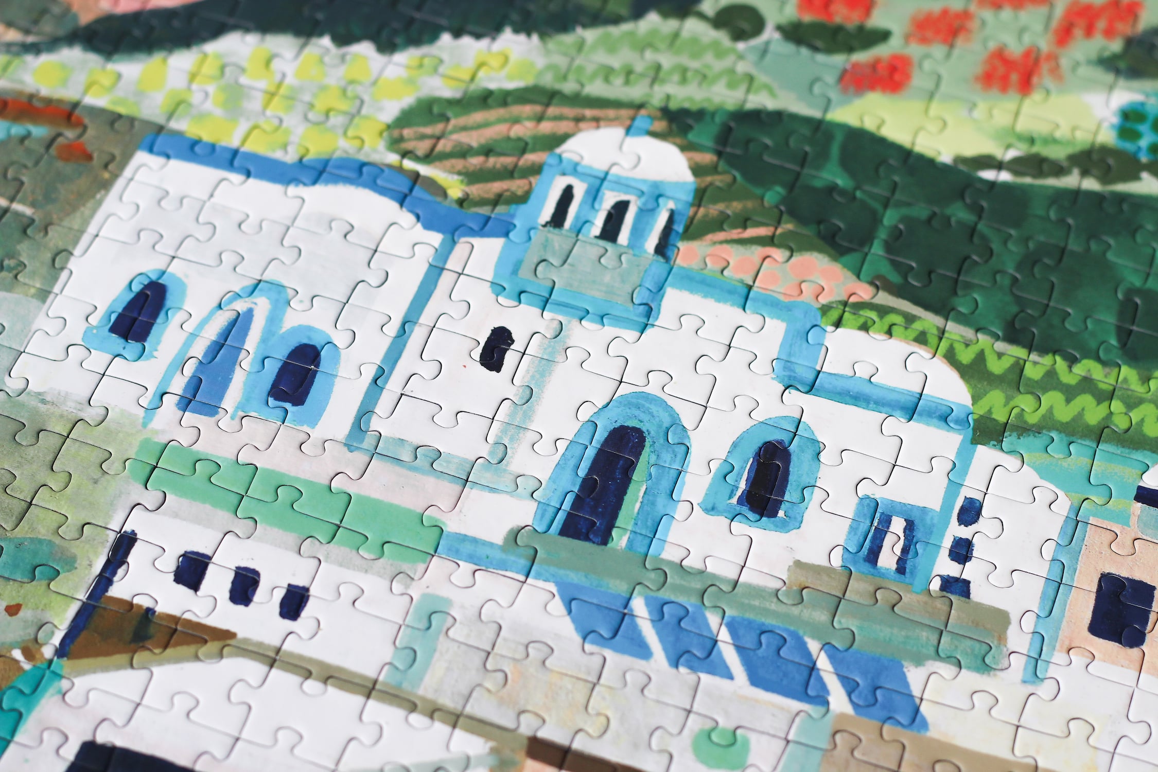 Außergewöhnliches 1000-Teile-Puzzle für Erwachsene, das einen Teil der griechischen Insel Milos zeigt. Zu sehen sind weiße Häuser and der Küste, Orangenbäume und Schiffe und Boote auf dem Meer.