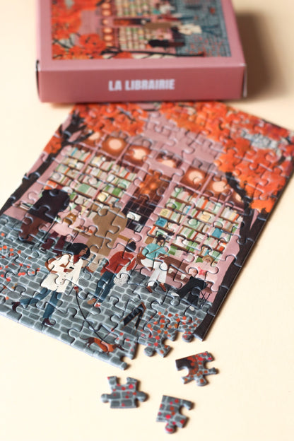 99-Teile-Mini-Puzzle „La Librairie“ von Piecely – Illustration einer herbstlichen Straßenszene vor einer Pariser Buchhandlung, auf rosafarbener Verpackung.