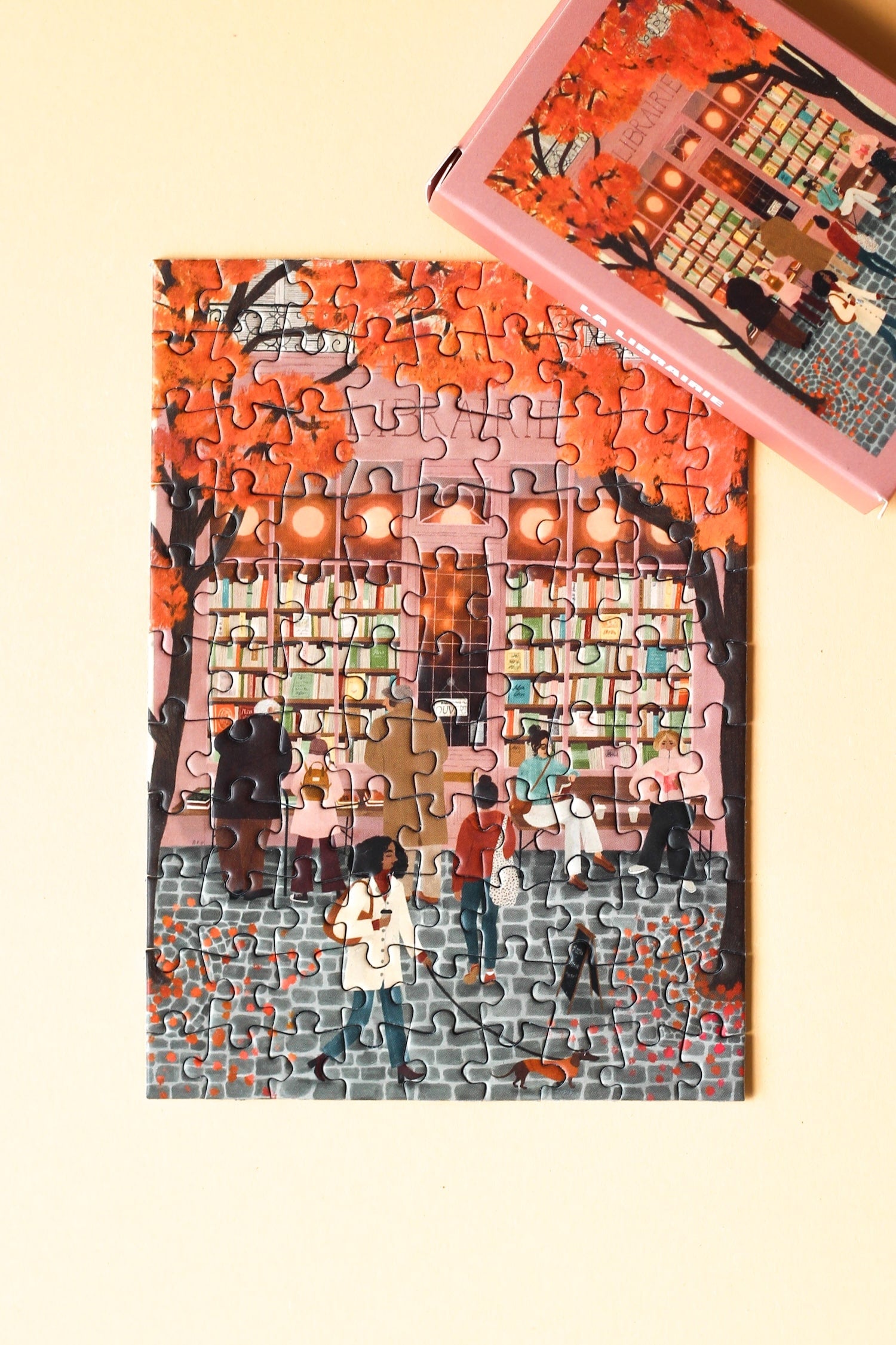 99-Teile-Mini-Puzzle „La Librairie“ von Piecely – Illustration einer herbstlichen Straßenszene vor einer Pariser Buchhandlung, auf rosafarbener Verpackung.