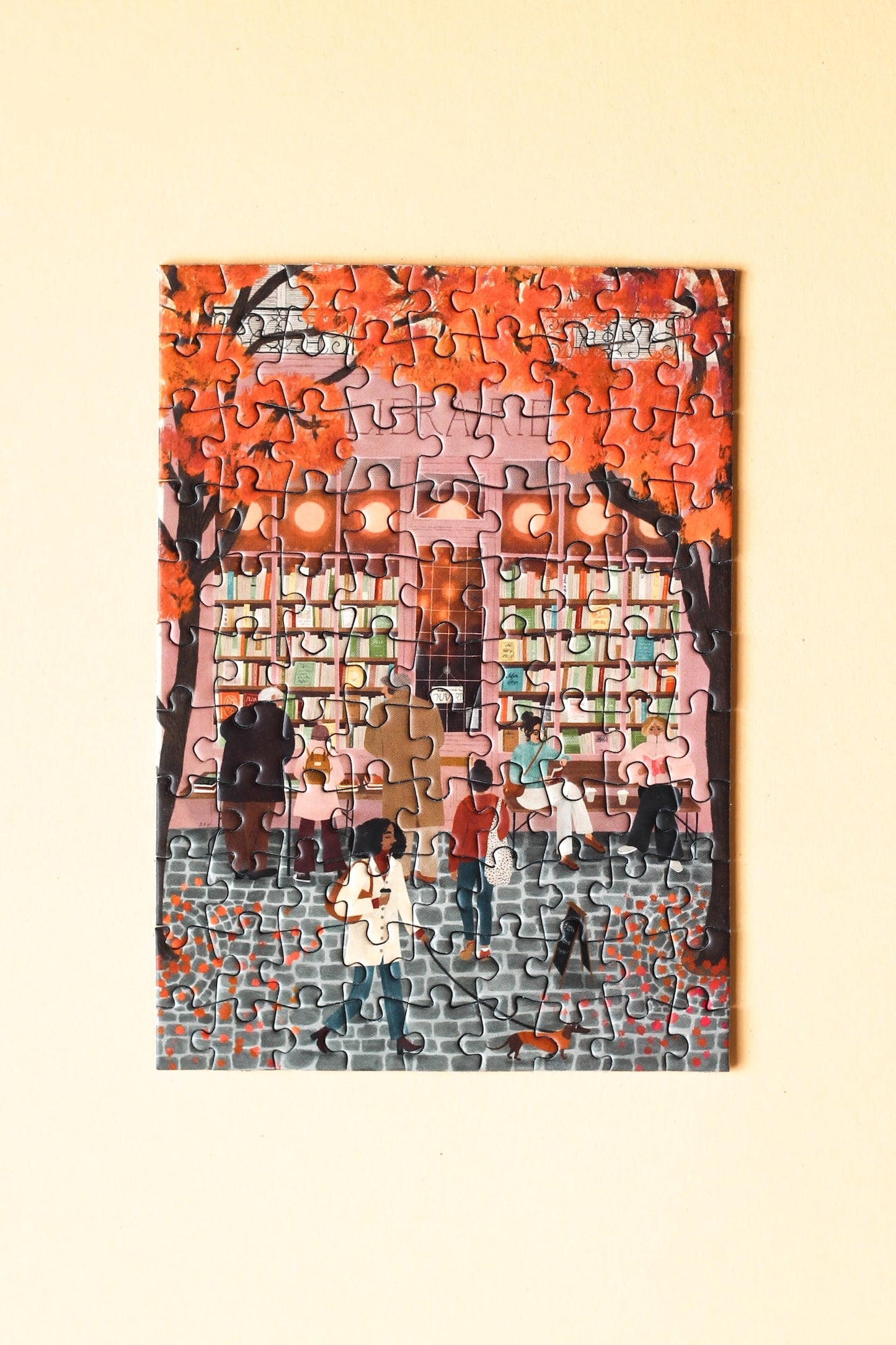 99-Teile-Mini-Puzzle „La Librairie“ von Piecely – Illustration einer herbstlichen Straßenszene vor einer Pariser Buchhandlung, auf rosafarbener Verpackung.