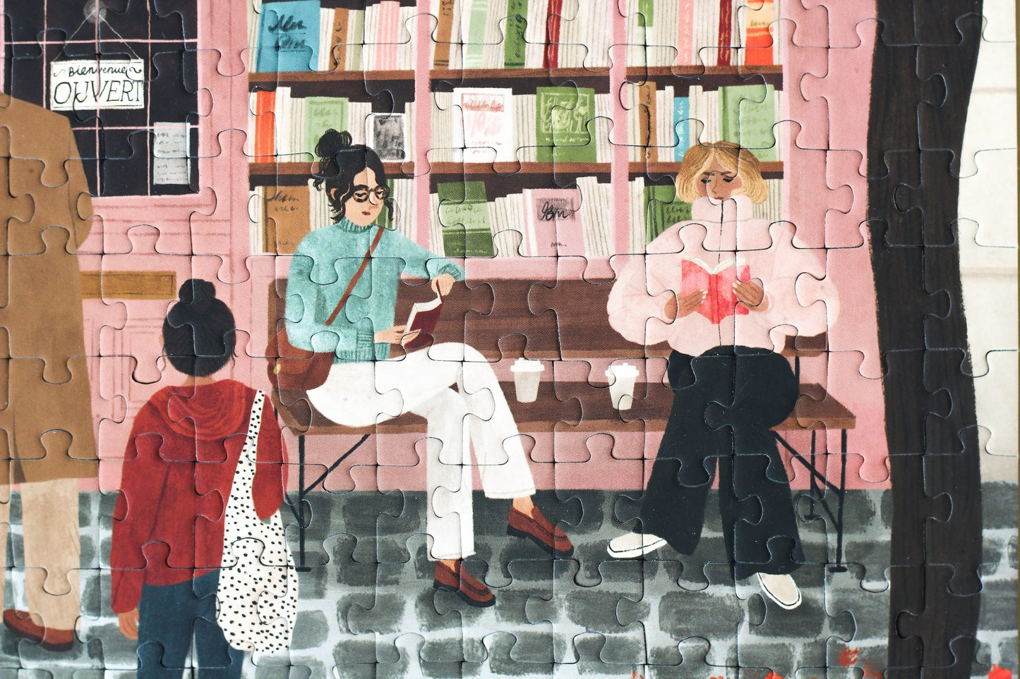 500-Teile-Puzzle „La Librairie“ von Piecely – Illustration einer herbstlichen Pariser Straßenszene vor einer kleinen Buchhandlung, auf rosa-brauner Verpackung.