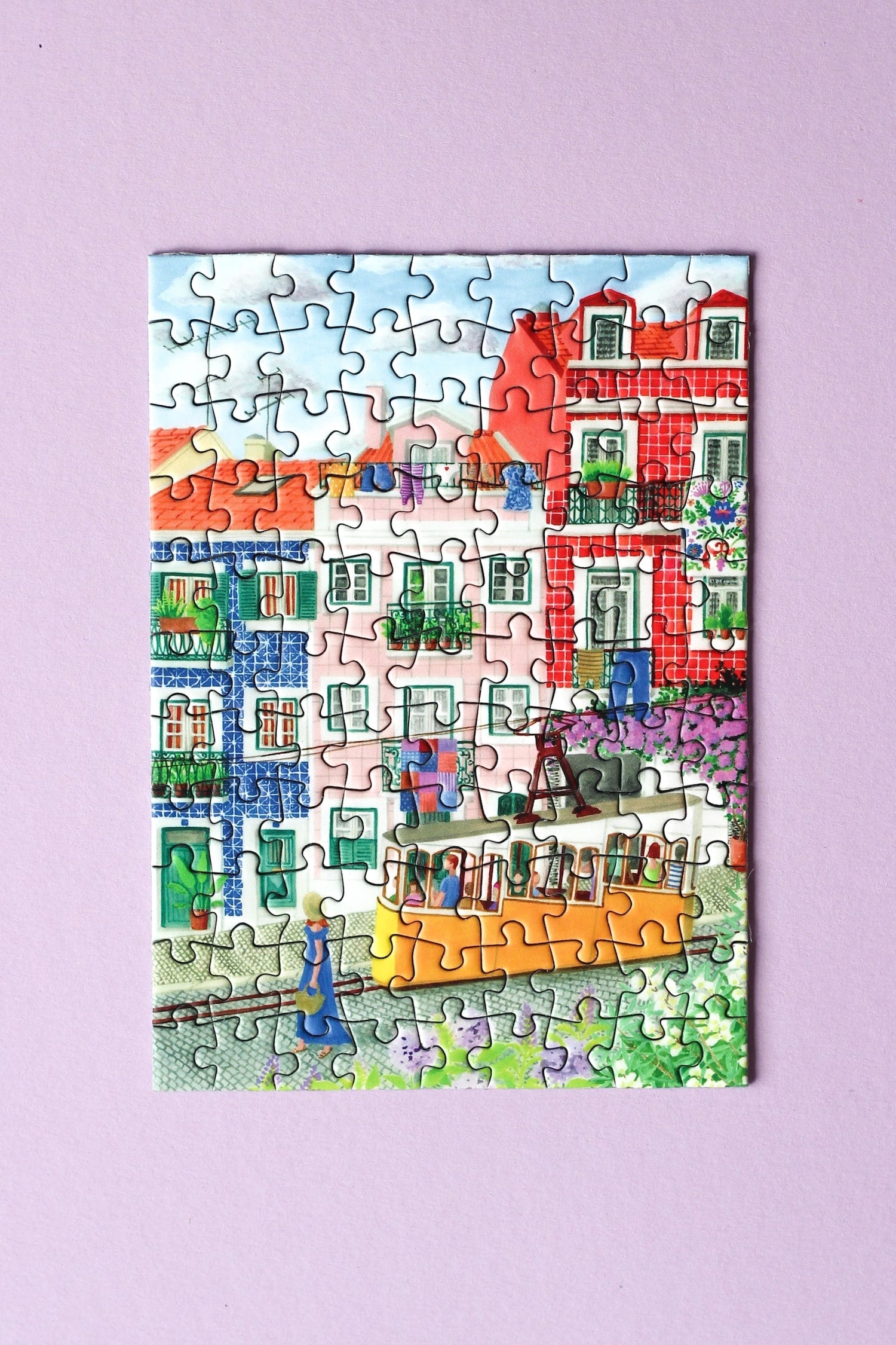 99-Teile-Mini-Puzzle „Lisbon“ von Piecely – Illustration einer farbenfrohen Straßenszene in Lissabon mit gelber Straßenbahn, auf pinker Verpackung.