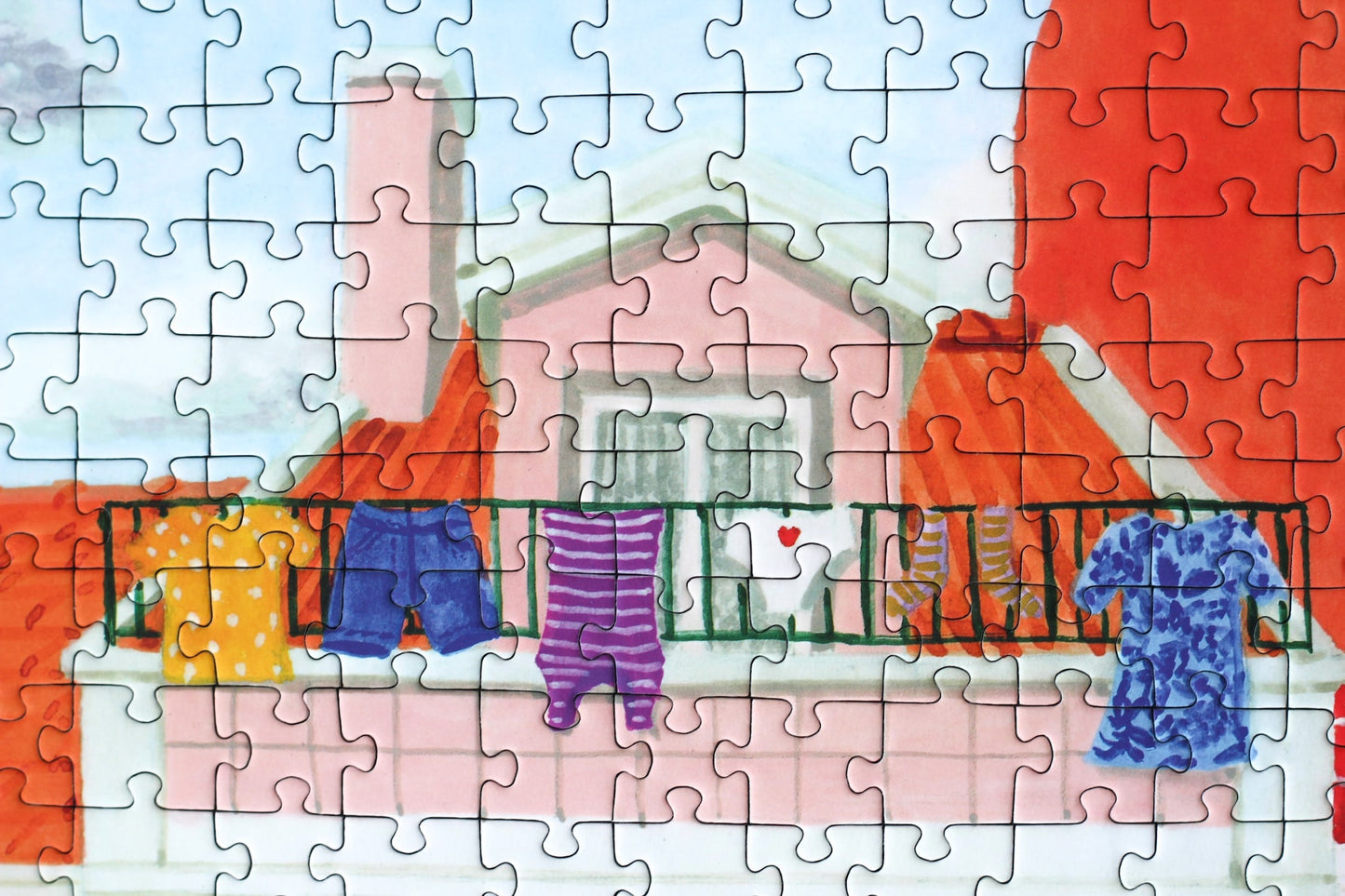 1000-Teile-Puzzle „Lisbon“ von Piecely – Illustration einer farbenfrohen Straßenszene in Lissabon mit gelber Straßenbahn und bunten Häusern, auf pinker Verpackung.