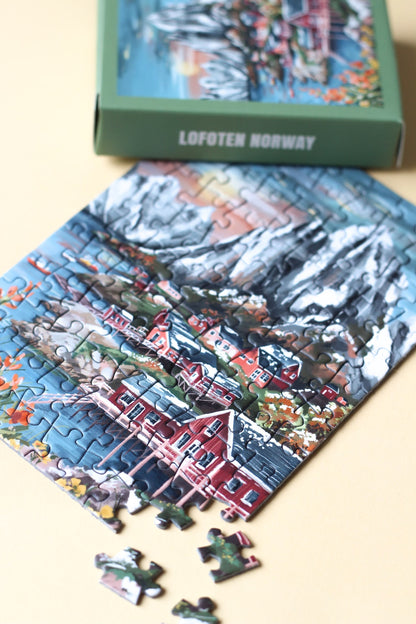 99-Teile-Mini-Puzzle „Lofoten Norway“ von Piecely – Illustration einer norwegischen Küstenlandschaft mit Bergen, roten Häusern und Meer, auf olivgrüner Verpackung.