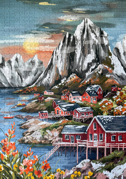 1000-Teile-Puzzle „Lofoten Norway“ von Piecely – Illustration einer norwegischen Küstenlandschaft mit schneebedeckten Bergen, roten Holzhäusern und Meer, auf olivgrüner Verpackung.