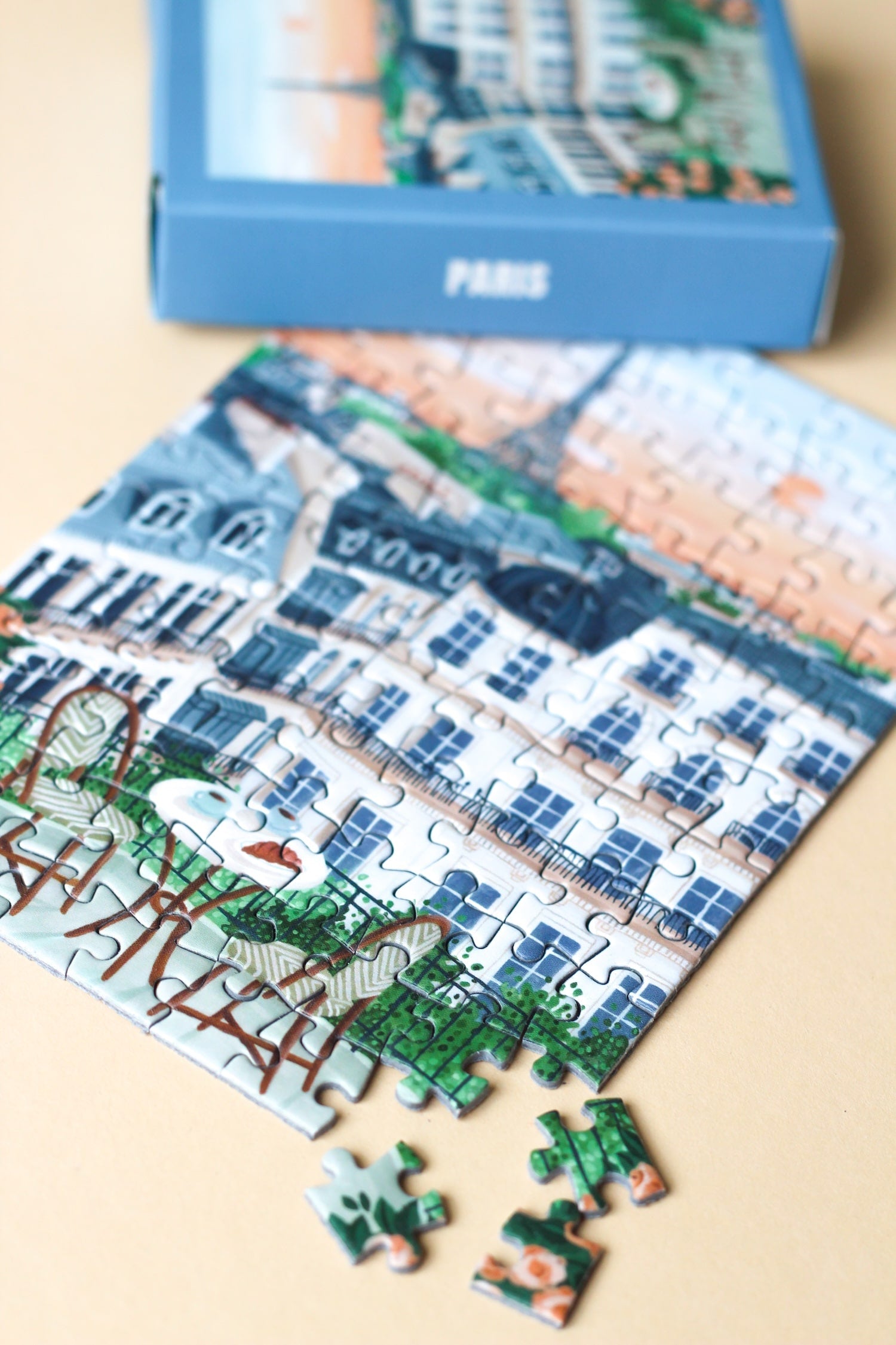 99-Teile-Mini-Puzzle „Paris“ von Piecely – Illustration eines Pariser Balkons mit Frühstückstisch, Rosen und Blick auf den Eiffelturm, auf hellblauer Verpackung.