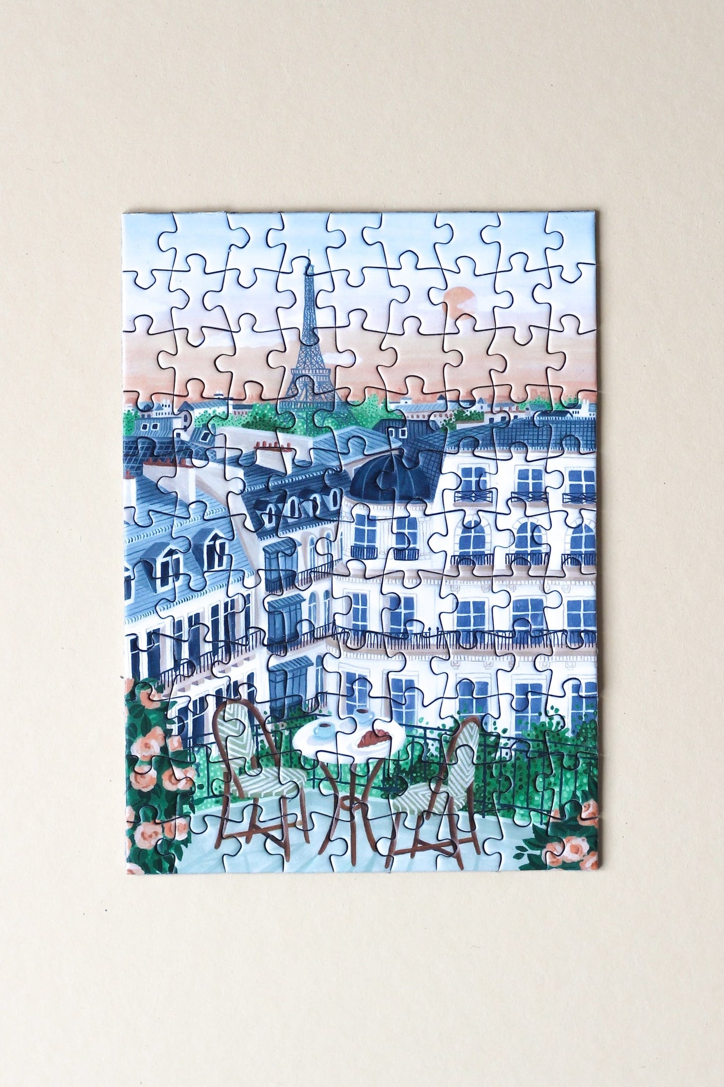 99-Teile-Mini-Puzzle „Paris“ von Piecely – Illustration eines Pariser Balkons mit Frühstückstisch, Rosen und Blick auf den Eiffelturm, auf hellblauer Verpackung.