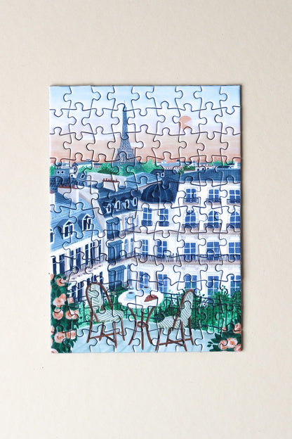 99-Teile-Mini-Puzzle „Paris“ von Piecely – Illustration eines Pariser Balkons mit Frühstückstisch, Rosen und Blick auf den Eiffelturm, auf hellblauer Verpackung.