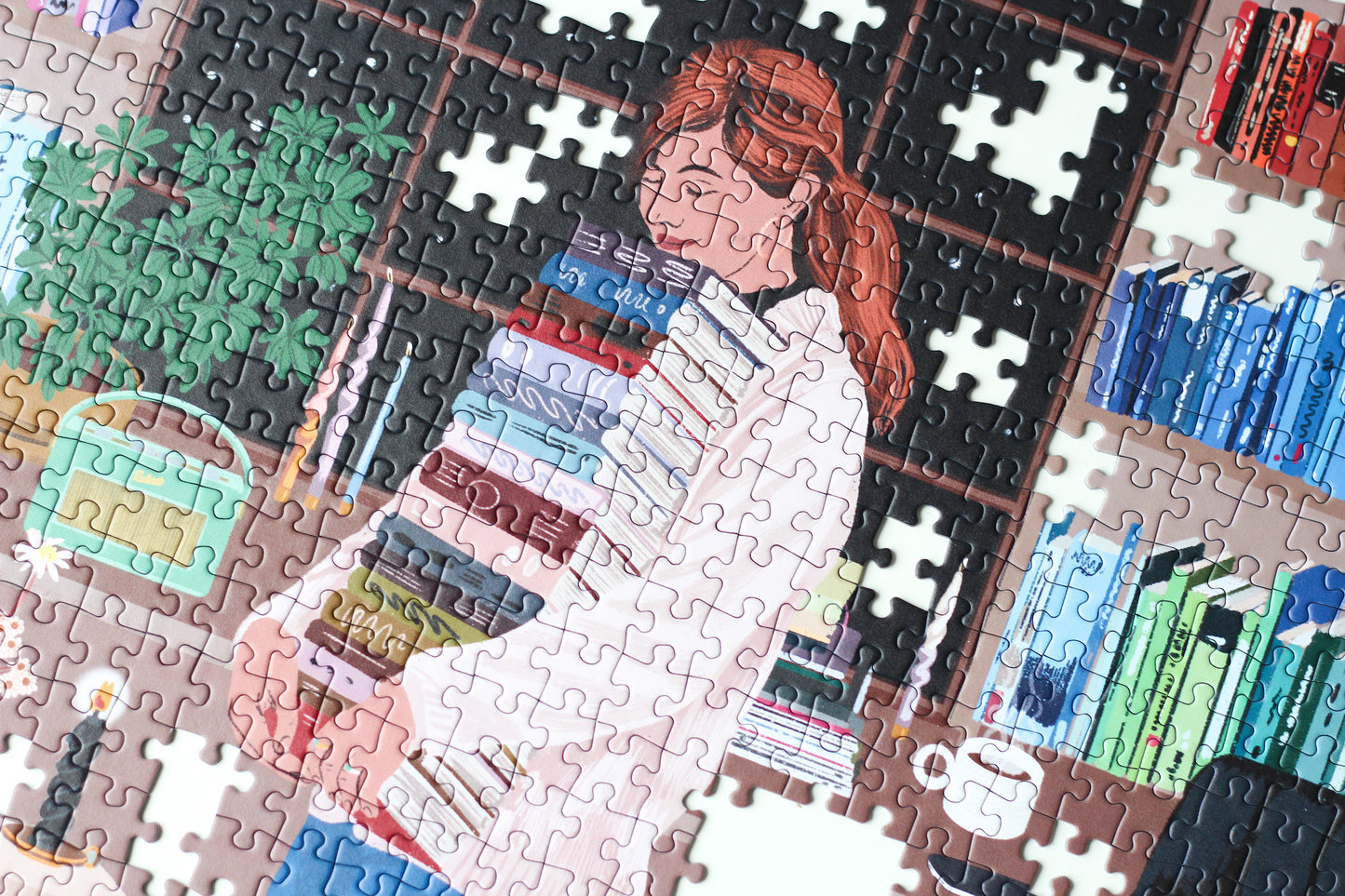 Nachhaltiges 1000-Teile-Puzzle, das eine Frau mit einem Stapel Bücher in der Hand zeigt. Im Hintergrund ist ein prall gefülltes Bücherregal und zwei süße Katzen.