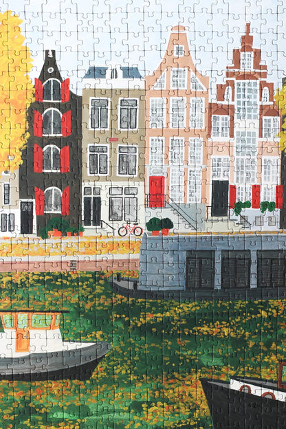 Plastikfreies Puzzle für Erwachsene, das eine Gracht in Amsterdam mit Häuserfassaden und Hausbooten im Herbst zeigt.