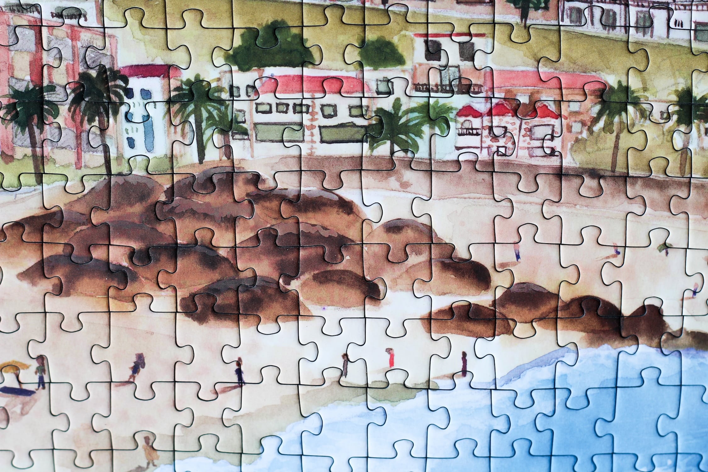 500-teiliges Puzzle für Erwachsene, das die Strandpromenade des Kapstädter Viertels Camps Bay zeigt. Im Vordergrund sind man Sandstrand und blaues Meer und im Hintergrund Häuserketten und die Berge.