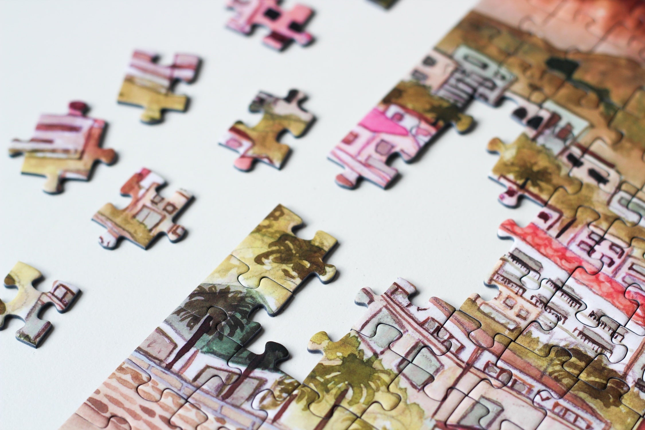 500-teiliges Puzzle für Erwachsene, das die Strandpromenade des Kapstädter Viertels Camps Bay zeigt. Im Vordergrund sind man Sandstrand und blaues Meer und im Hintergrund Häuserketten und die Berge.