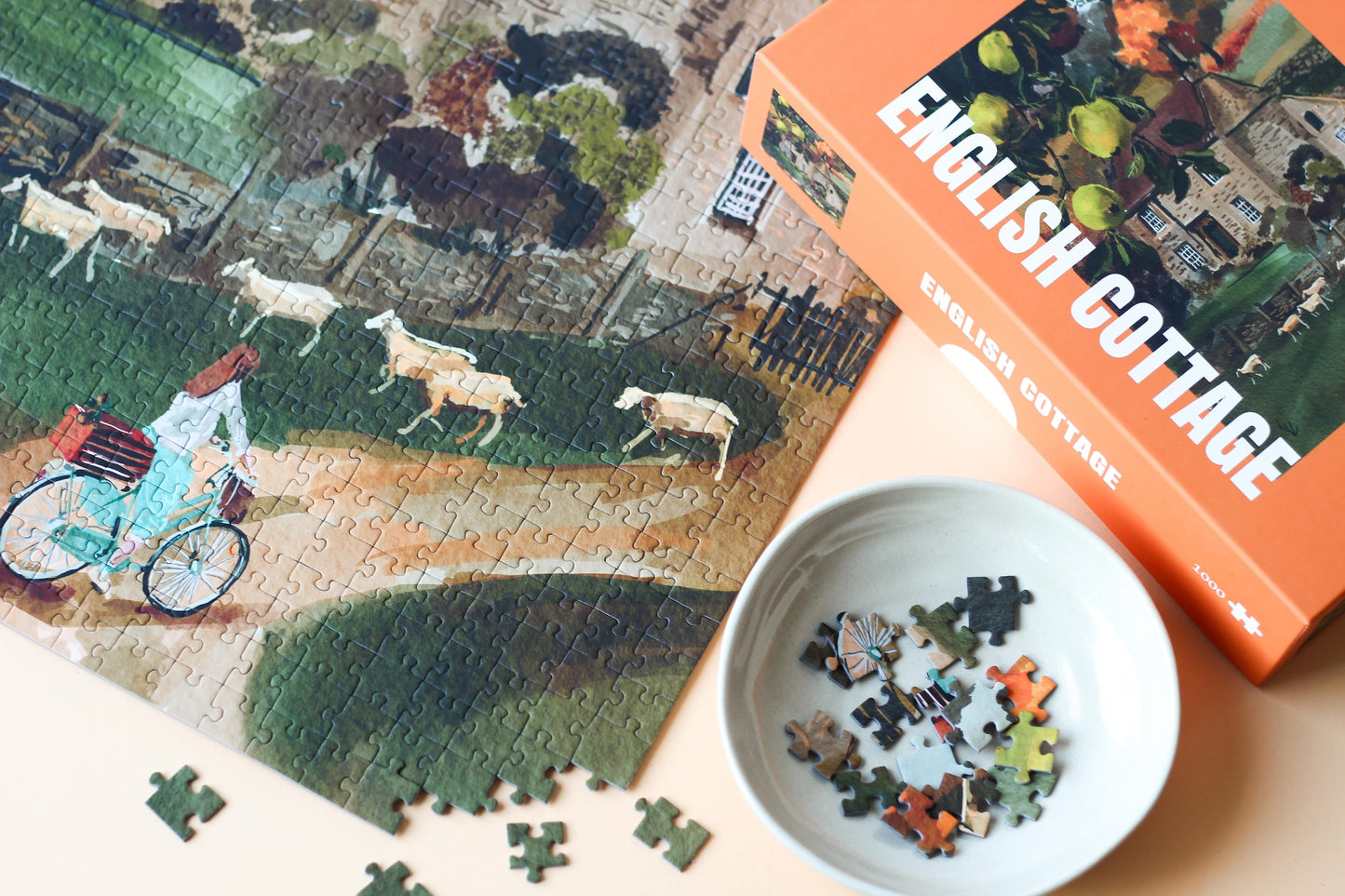 Plastikfreies Puzzle für Erwachsene, das ein Cottage auf dem englischen Land im Herbst zeigt. Vor dem Cottage stehen ein Birnbaum und eine Schafherde. Eine Frau fährt auf einem Fahrrad den Weg zum Cottage hoch.