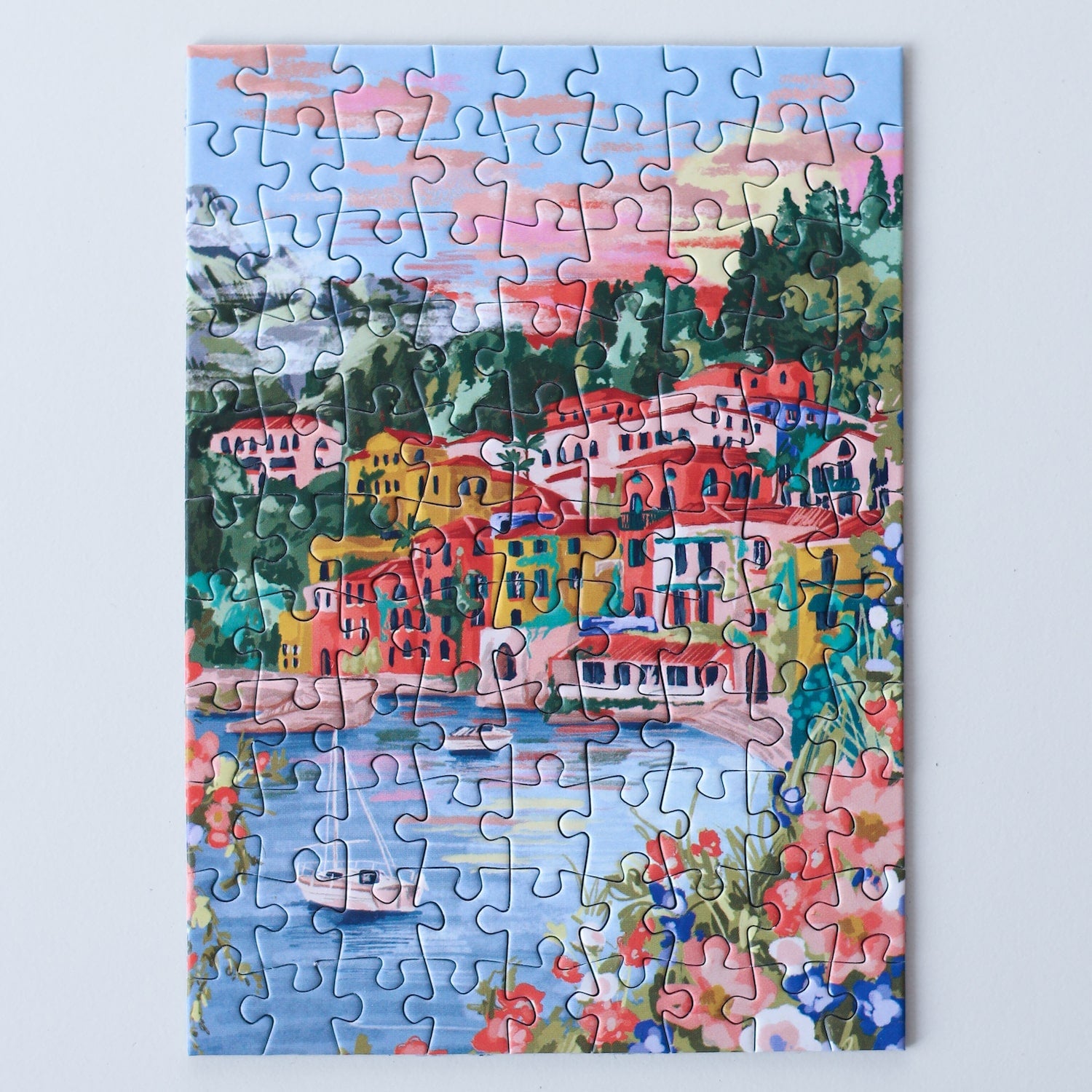 99-teiliges Minipuzzle für Erwachsene, das den Comer See in Varenna zeigt. In der Bucht befinden sich zwei Boote und die Sicht auf den See ist gesäumt von bunten Häusern.