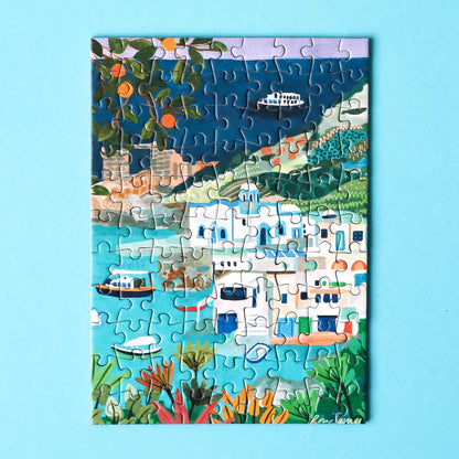 Plastikfreies Minipuzzle, das die Küste der Insel Milos in Griechenland zeigt. Zu sehen sind weiße Häuser, blaues Meer, saftige Orangen und Schiffe