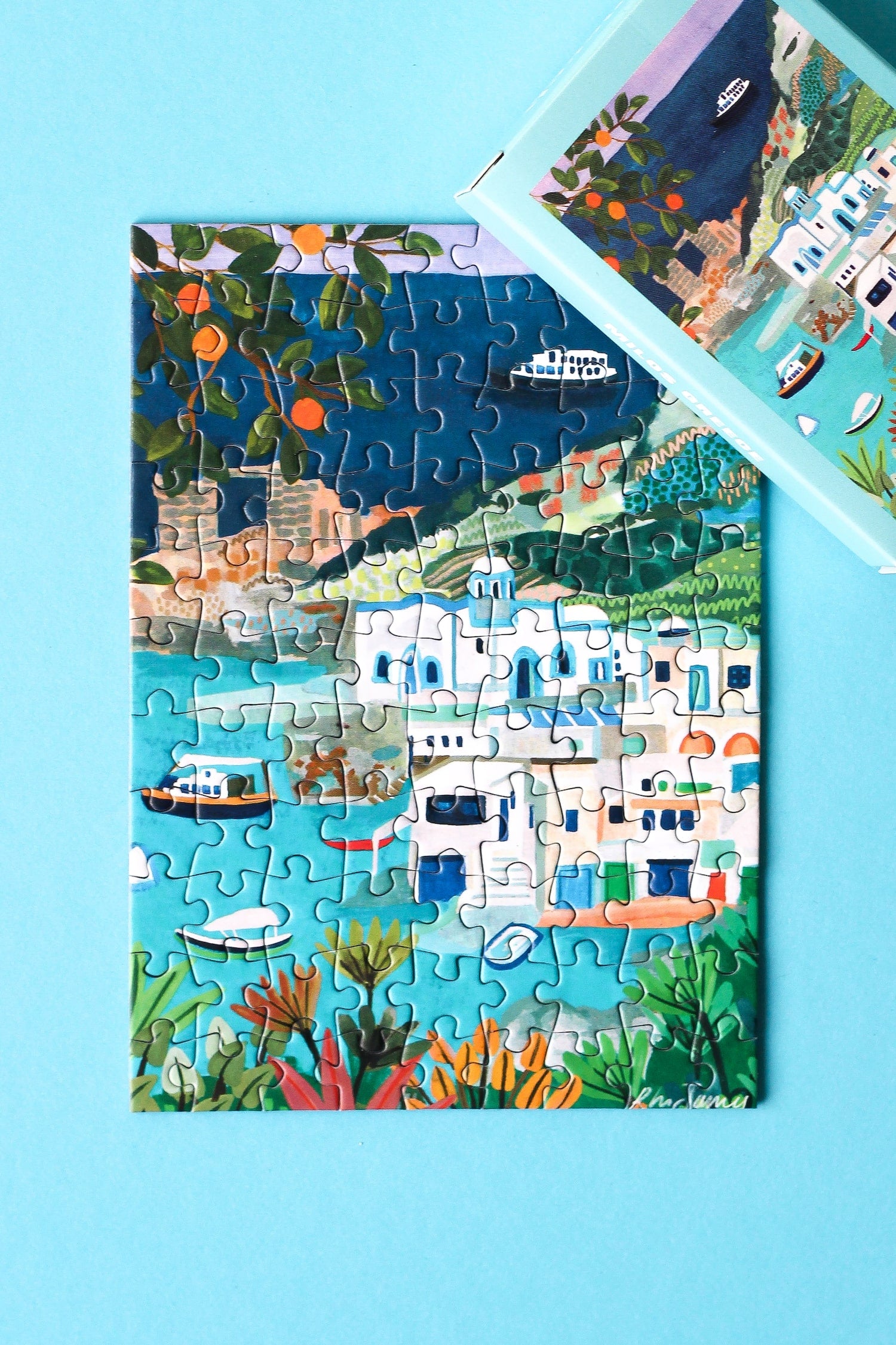 Plastikfreies Minipuzzle, das die Küste der Insel Milos in Griechenland zeigt. Zu sehen sind weiße Häuser, blaues Meer, saftige Orangen und Schiffe