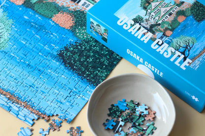 Plastikfreies Puzzle für Erwachsene, das die Burg Osaka in Japan in pastelligen Blau- und Grüntönen zeigt. 