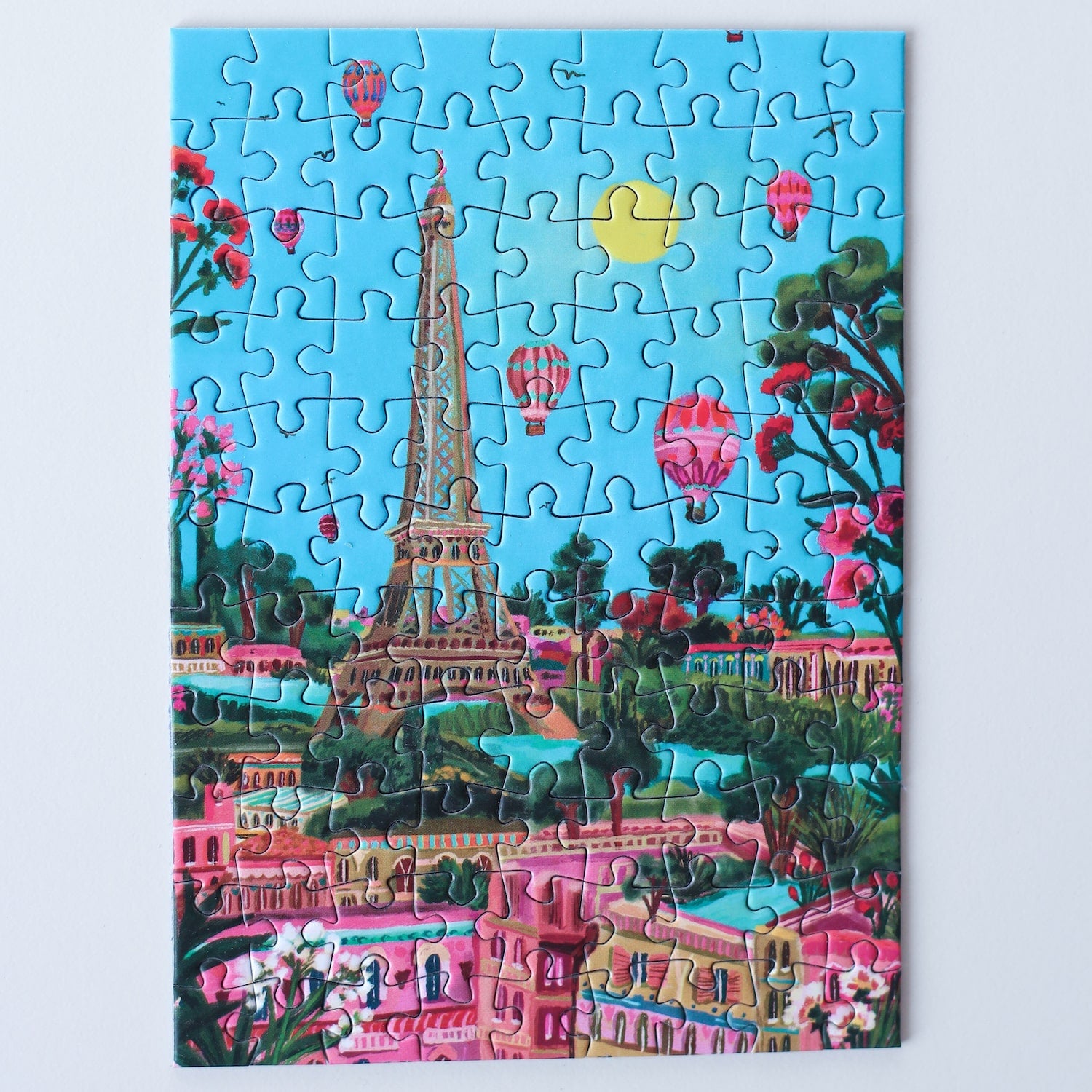 99-teiliges Minipuzzle für Erwachsene, das den Eiffelturm in Paris zeigt. Die Sonne scheint, der Himmel ist blau und ind er Luft befinden sich mehrere Heißluftballons.