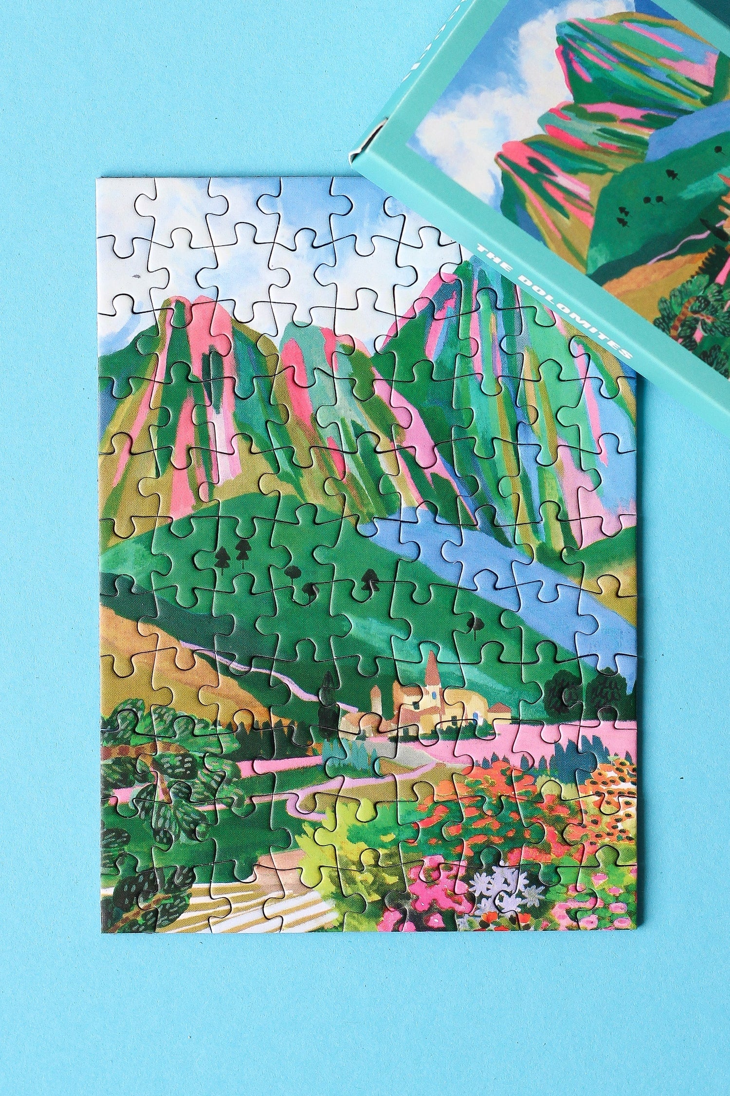 Plastikfreies Minipuzzle für Erwachsene, das die Dolomiten in Italien zeigt. Zu sehen sind ein kleines Dorf, die Berge und ein buntes Blumenmeer