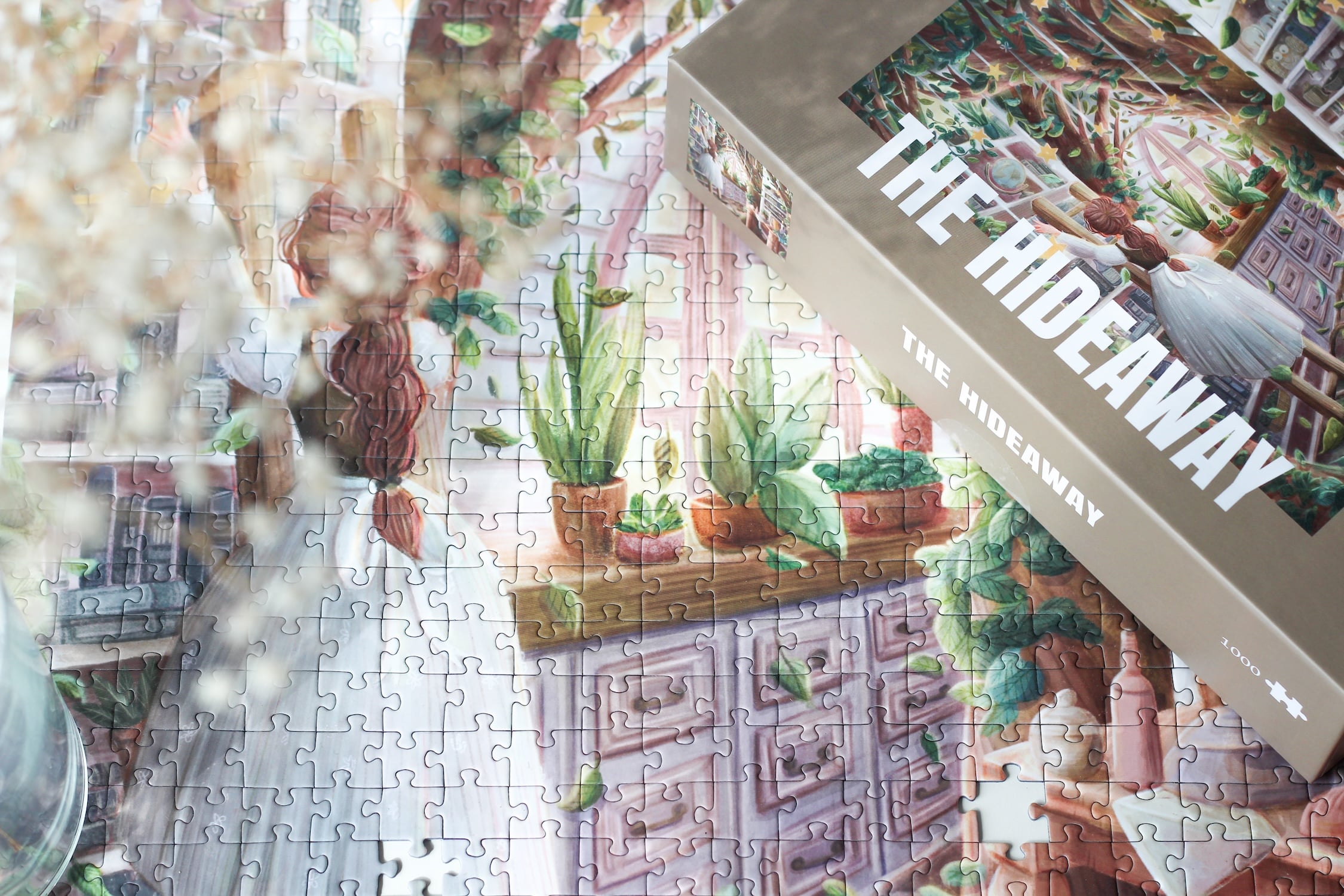 1000-teiliges Puzzle für Erwachsene, das eine Frau auf einer Leiter in einer verwunschenen Küche zeigt. Mitten in der Küche wächst ein Baum und die Regale sind gefüllt mit Büchern, Porzellan und Pflanzen.