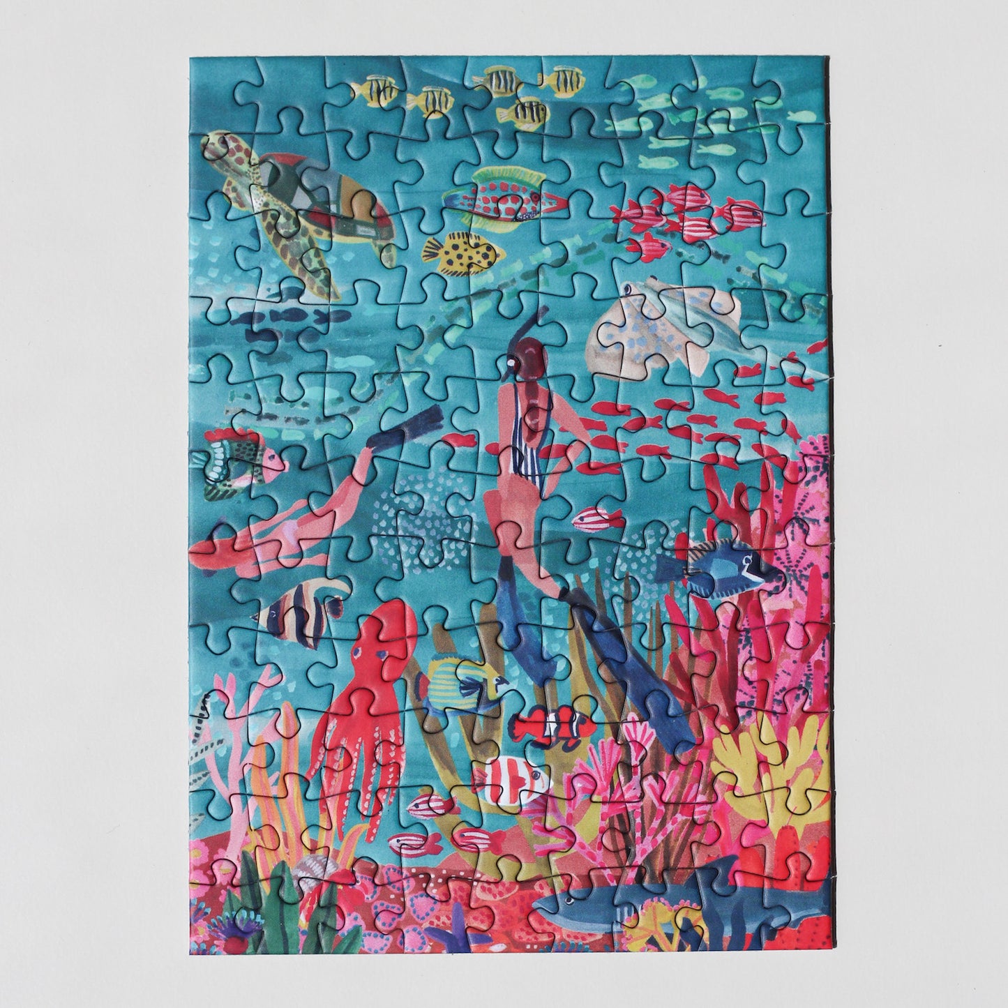 99-teiliges Under The Sea Minipuzzle für Erwachsene, das zwei Frauen beim Schnorcheln im Meer zeigt. Die Frauen sind umgeben von bunten Fischen, einem Oktopus, einem Rochen, einer Schildkröte und einem Hai. 