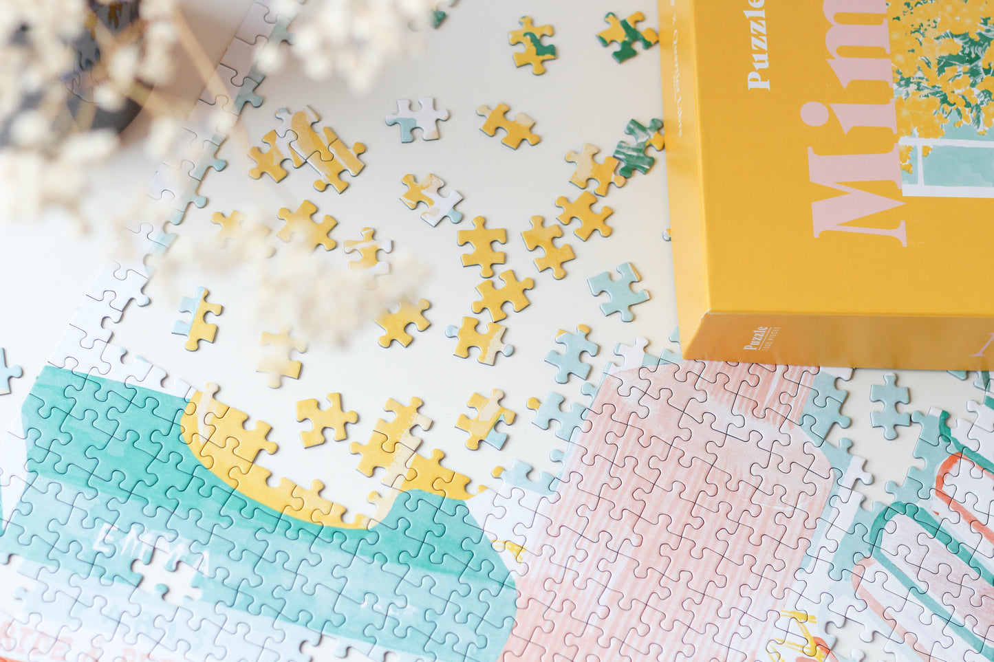 Nachhaltiges, 1000-teiliges Puzzle für Erwachsene, das ein Stillleben bestehend aus einem Strauß Mimosen, einer Tasse Kaffee und Büchern zeigt.